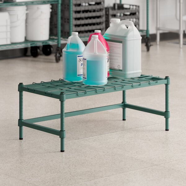 A green metal Regency dunnage rack with bottles on it.