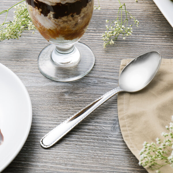 A Reed & Barton Stitch dessert spoon next to a glass of dessert on a table.