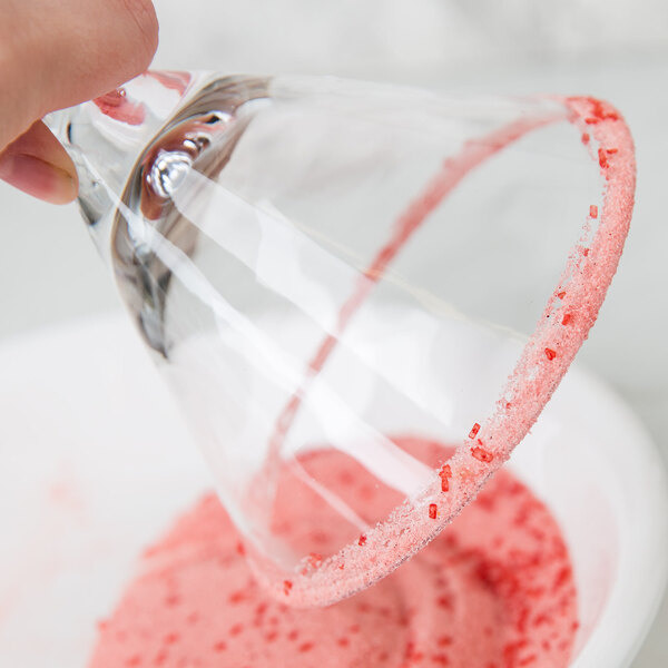 A hand holding a glass with a pink rim of Rokz Cranberry Cosmo Cocktail.