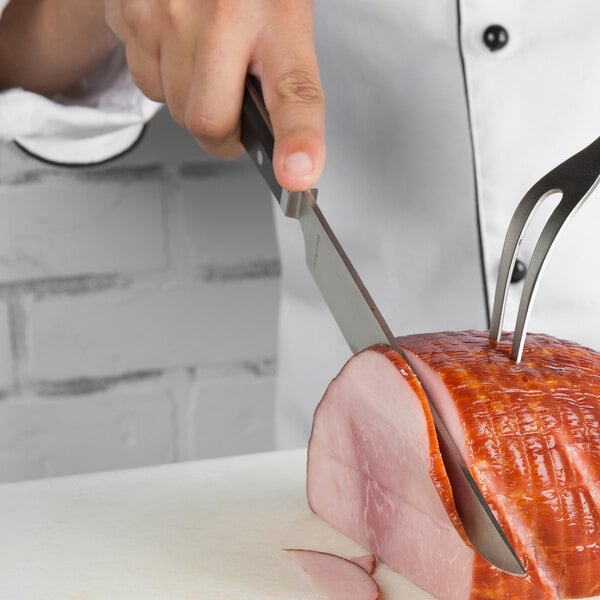 A person using a Reed & Barton stainless steel carving knife to cut a ham.