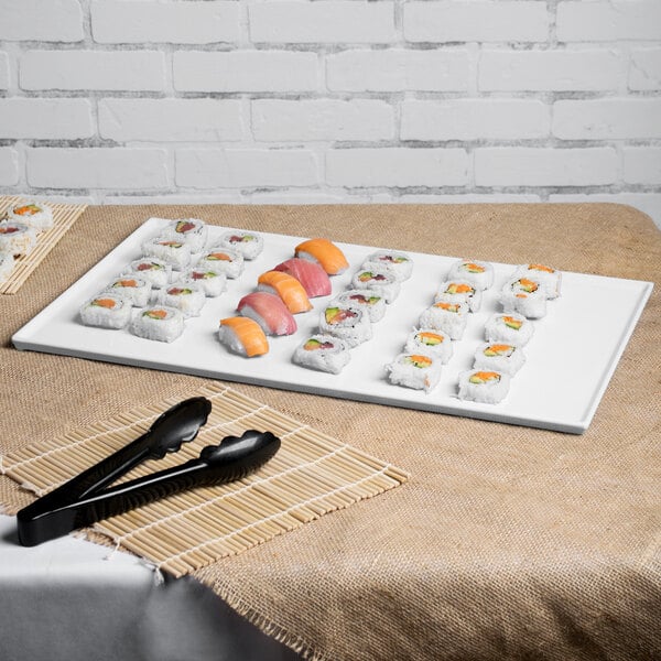 A Tablecraft white cast aluminum rectangular cooling platter on a table with sushi on it.