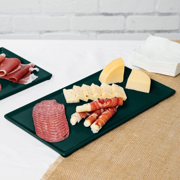 Two hunter green Tablecraft cast aluminum cooling platters with food on a table.