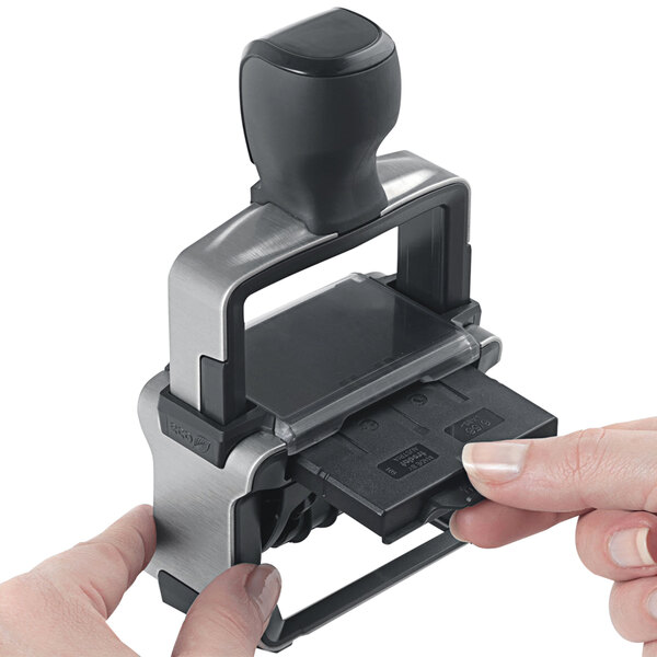 A person's hand using a Trodat black self-inking date stamp.