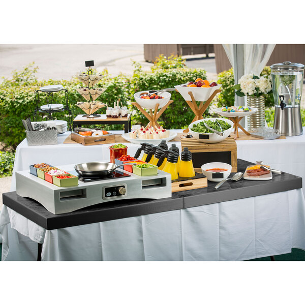 A Tablecraft translucent black metal table cover on a table with food and drinks on it.