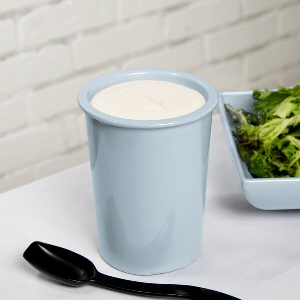 A gray Tablecraft salad dressing crock with white liquid in it on a bowl of salad.