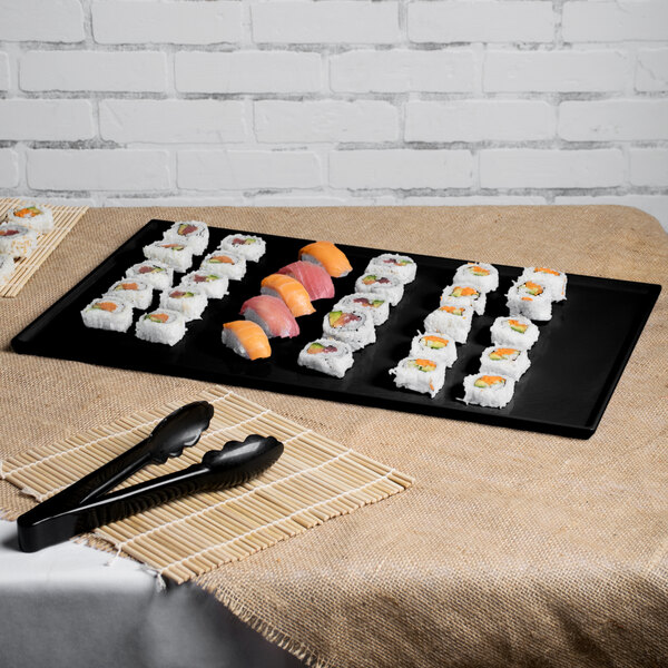 A black Tablecraft rectangular cast aluminum cooling platter with sushi on it.