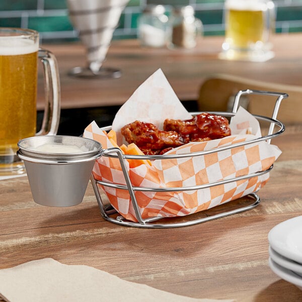 A Clipper Mill stainless steel oval basket with a ramekin holder filled with chicken wings and sauce on a table.