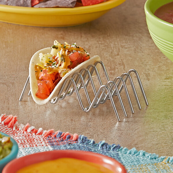 A taco on a stainless steel Clipper Mill by GET taco holder on a table with other food.