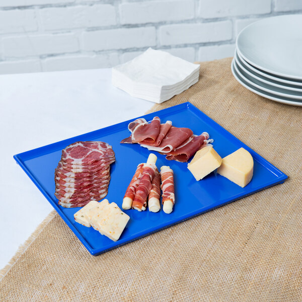 A Tablecraft cobalt blue rectangular cast aluminum platter with meat and cheese on a blue surface.