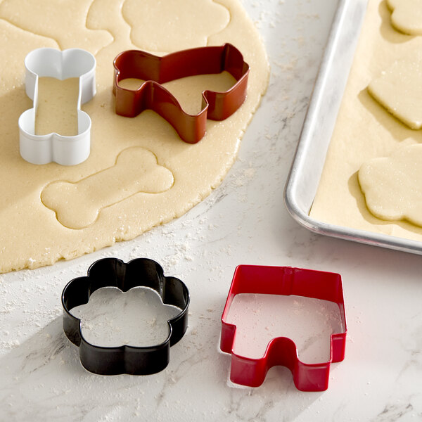A set of four metal cookie cutters in pet-themed shapes, including a bone, a dog, a paw, and a dog house.