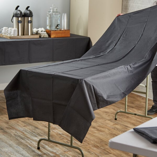 A man using a Hoffmaster black linen-like table cover to set up a table outdoors.