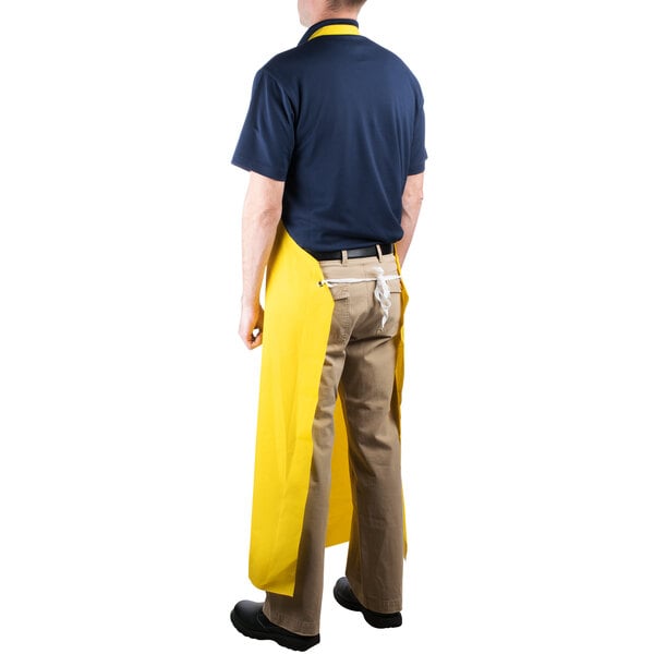 A man wearing a yellow Cordova polyester dishwasher apron standing in a professional kitchen.