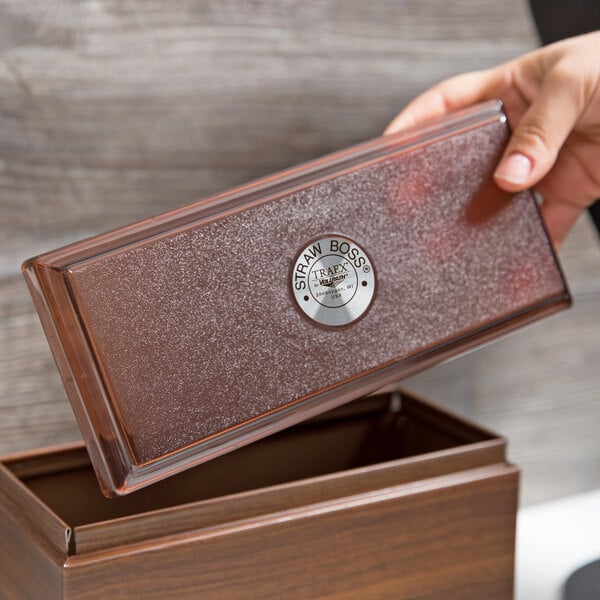 A hand holding a brown box with a Vollrath Straw Boss lid.