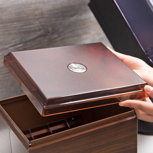 A hand holding a brown box with a Vollrath Straw Boss dispenser lid.