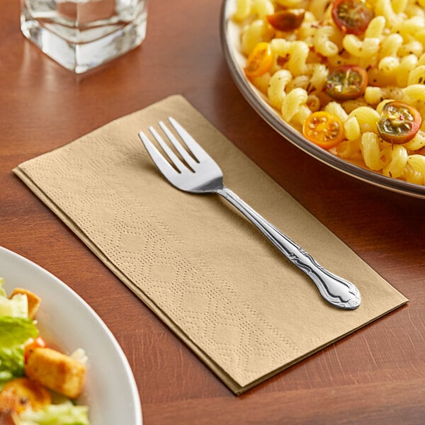 A Hoffmaster beige 2-ply paper dinner napkin with a fork on it next to a plate of pasta.