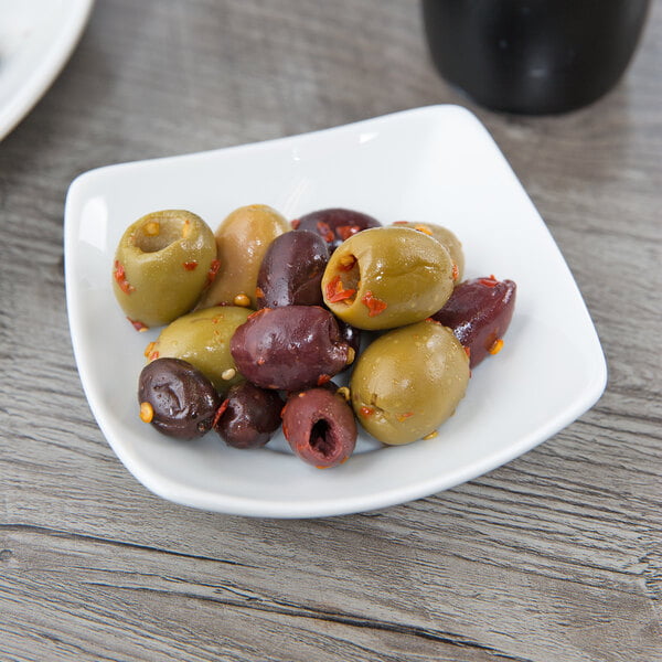 A Schonwald square porcelain bowl filled with green olives on a table.