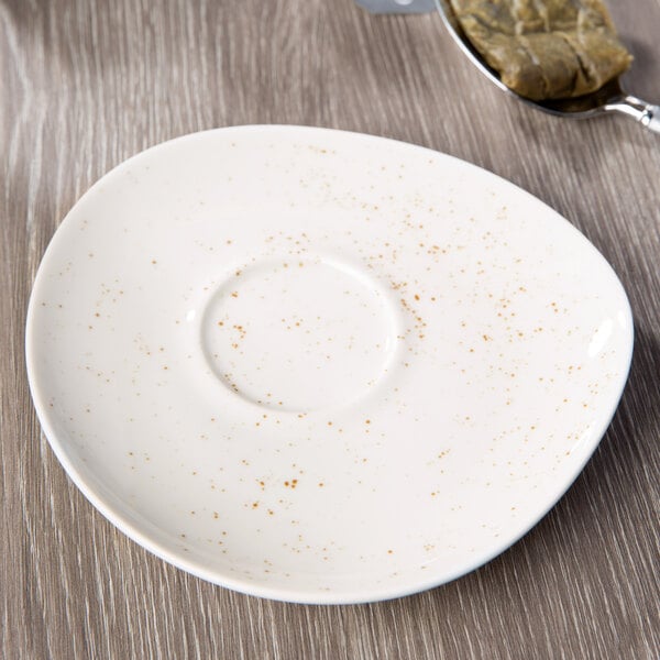 A Schonwald white porcelain saucer with brown specks next to a spoon.