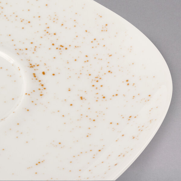 A white porcelain saucer with orange speckled spots.