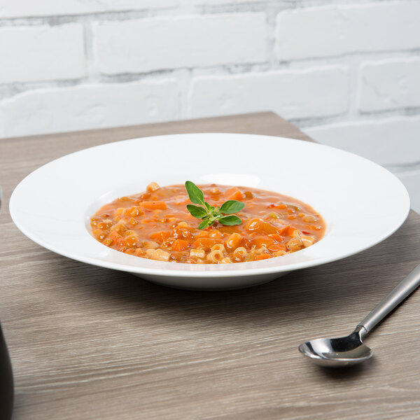 A Schonwald white porcelain bowl of soup with a spoon on a table.