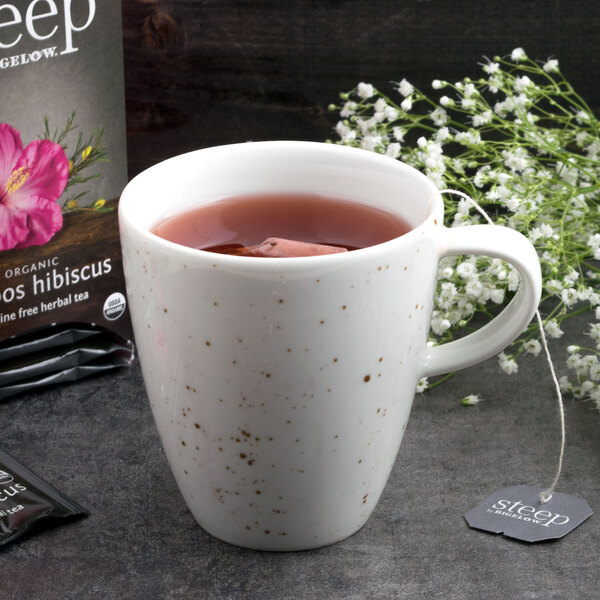 A Schonwald white porcelain cup of tea with a tea bag in it next to a box of tea.
