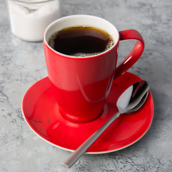 A red Schonwald porcelain mug with a spoon on a saucer.