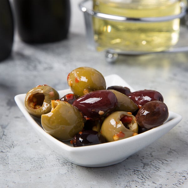 A white square sauce cup filled with green olives.