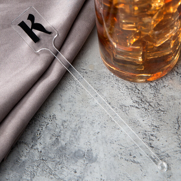 A WNA Comet clear plastic rectangular stirrer in a glass of liquid.