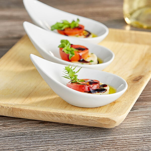 A wooden tray with three white porcelain tasting spoons with food in them.