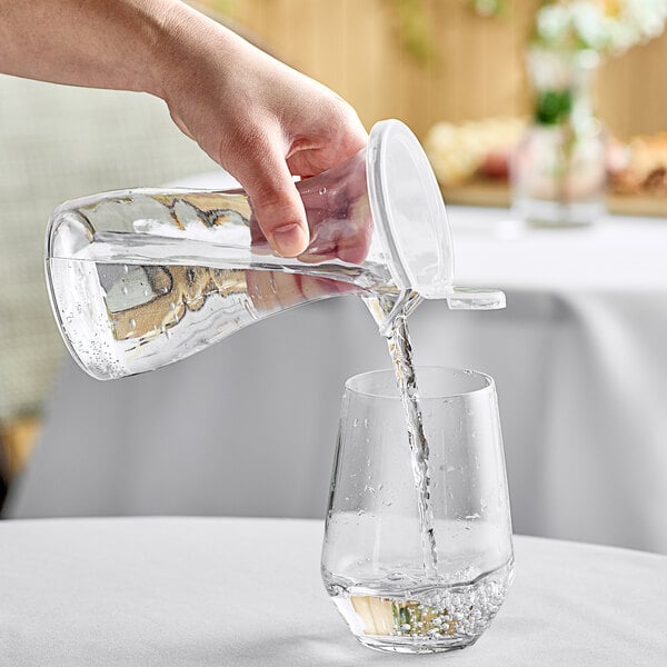 A hand pouring water into a GET polycarbonate decanter on a table.