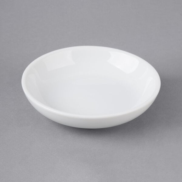 A Choice bright white porcelain round sauce cup on a gray surface.