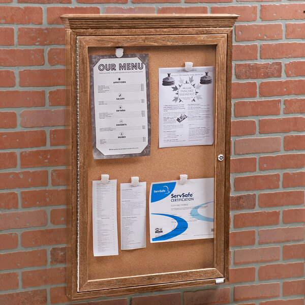 An Aarco natural oak enclosed bulletin board with cork papers attached.