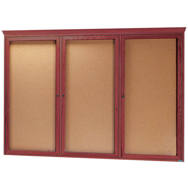 An Aarco cherry enclosed cork bulletin board with three glass doors.
