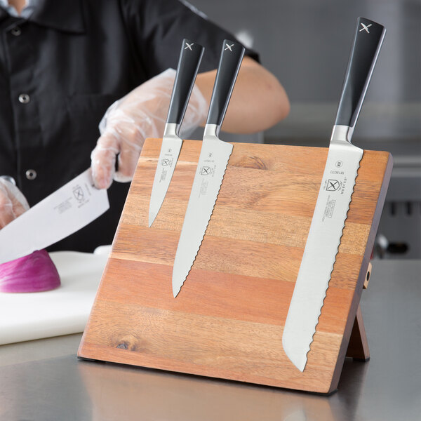 A person holding a Mercer Culinary ZüM® knife on a wooden board.