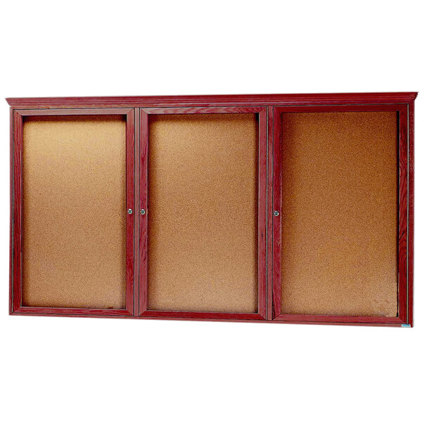 An Aarco cherry wood bulletin board with three doors enclosing cork boards.