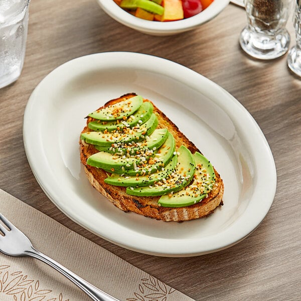 An Acopa narrow rim oval stoneware platter with a knife and fork on a table next to a napkin and plate of food.