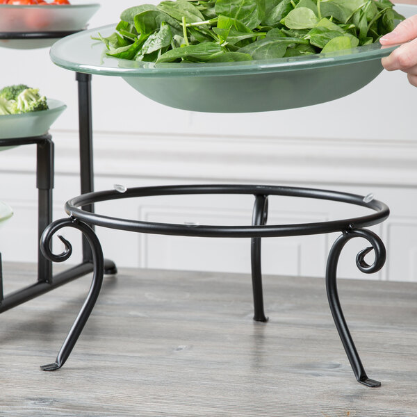 A black Libbey metal display frame holding a bowl of spinach on a wood table.