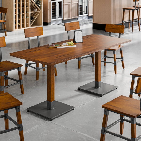 A rectangular solid wood live edge table top with a rustic walnut finish, set on metal bases and surrounded by matching wooden chairs in a dining area.