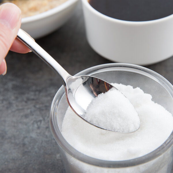 A hand holding a Libbey stainless steel teaspoon over a bowl of sugar.