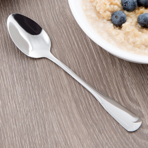 A World Tableware stainless steel teaspoon on a table next to a bowl of oatmeal with blueberries.