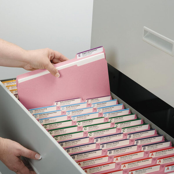 A person opening a file cabinet with a pink Smead file folder.