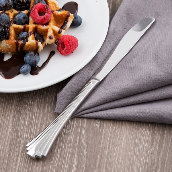 A plate of waffles with berries and chocolate sauce with a Libbey stainless steel dinner knife on a napkin.