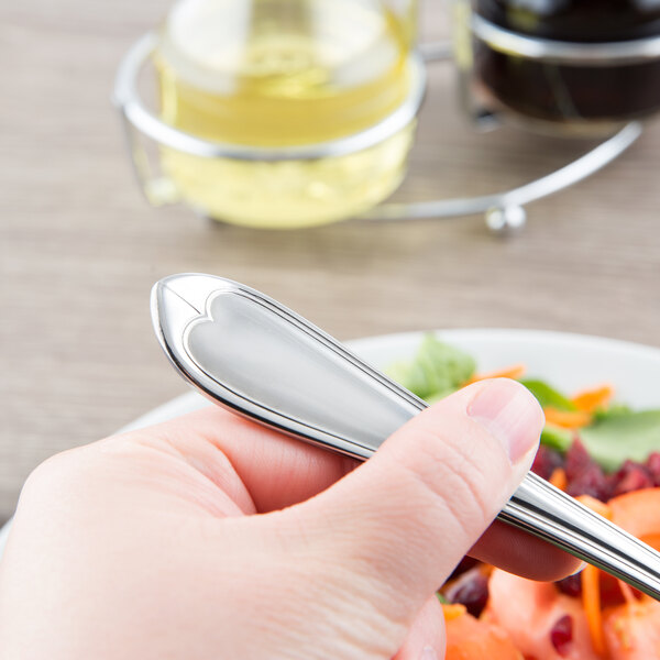 A hand holding a Libbey stainless steel salad fork over a plate of salad.