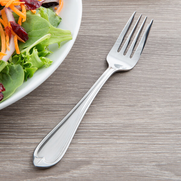 A Libbey stainless steel salad fork next to a plate of salad.