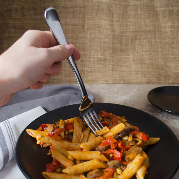 A hand holding a Libbey Auberge stainless steel dinner fork over a plate of pasta.