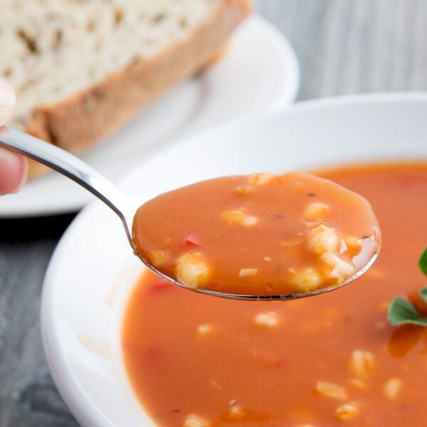 A World Tableware Columbus stainless steel bouillon spoon filled with soup in a bowl.
