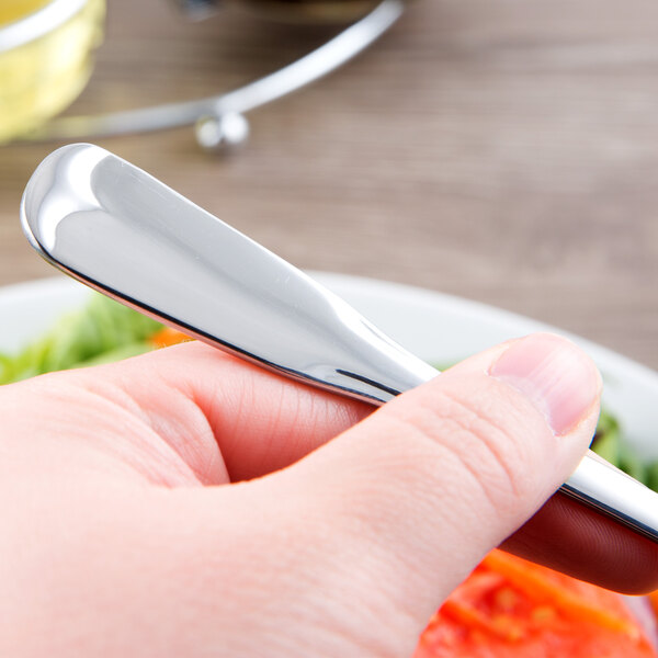A person holding a World Tableware Columbus stainless steel salad fork over a plate of food.