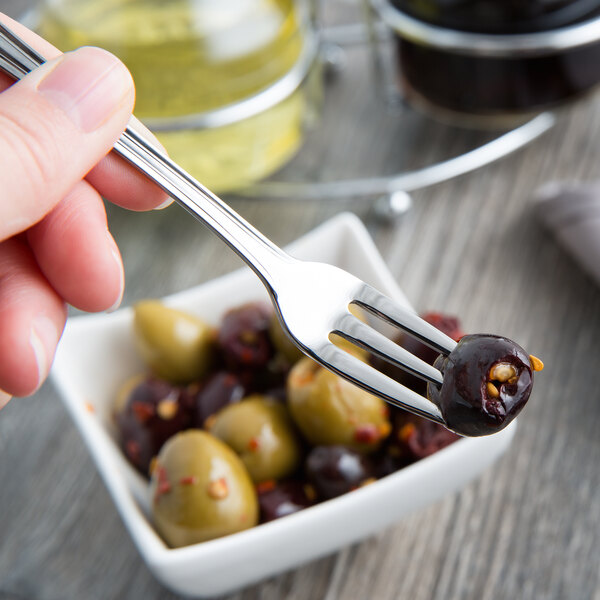 A Libbey stainless steel cocktail fork holding a black olive.