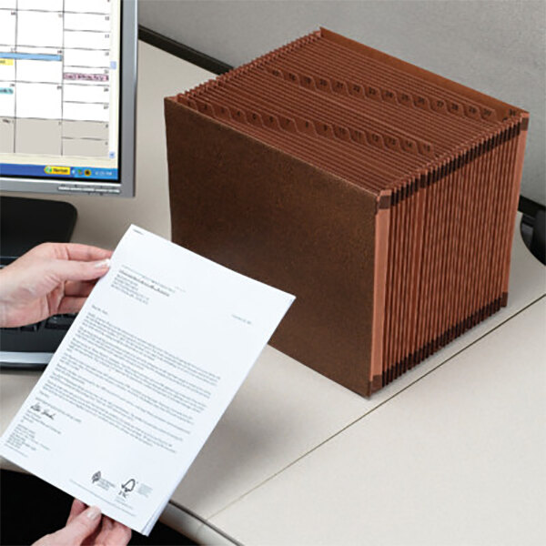 A person using a Smead TUFF legal size file folder to organize documents on a white table.