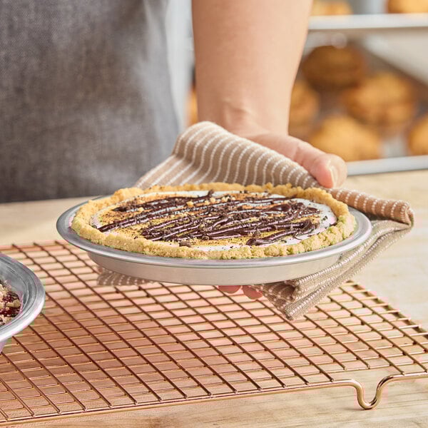 An aluminum pie pan holding a pie with a graham cracker crust and chocolate drizzle.