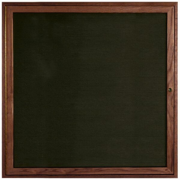 An Aarco enclosed bulletin board with a walnut frame and black felt.